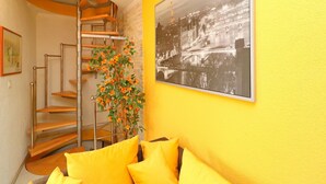 Una habitación con una escalera de caracol, un cuadro grande enmarco de una vista urbana y una planta con flores naranjas.