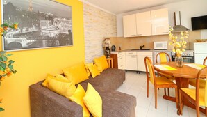 Una sala de estar moderna con sofá y cojines amarillos, un comedor con mesa y sillas de madera, una cocina con armarios blancos, y una fotografía en blanco y negro de un paisaje urbano.