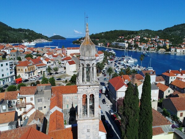 Un pueblo costero con una iglesia destacada que cuenta con un alto campanario, rodeado de edificios residenciales y un puerto deportivo.