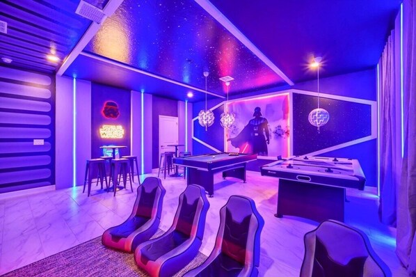 A room with a pool table, foosball table, and gaming chairs.