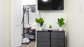 Una habitación con un televisor montado en la pared, un mueble negro con cajones y dos plantas en macetas encima.
