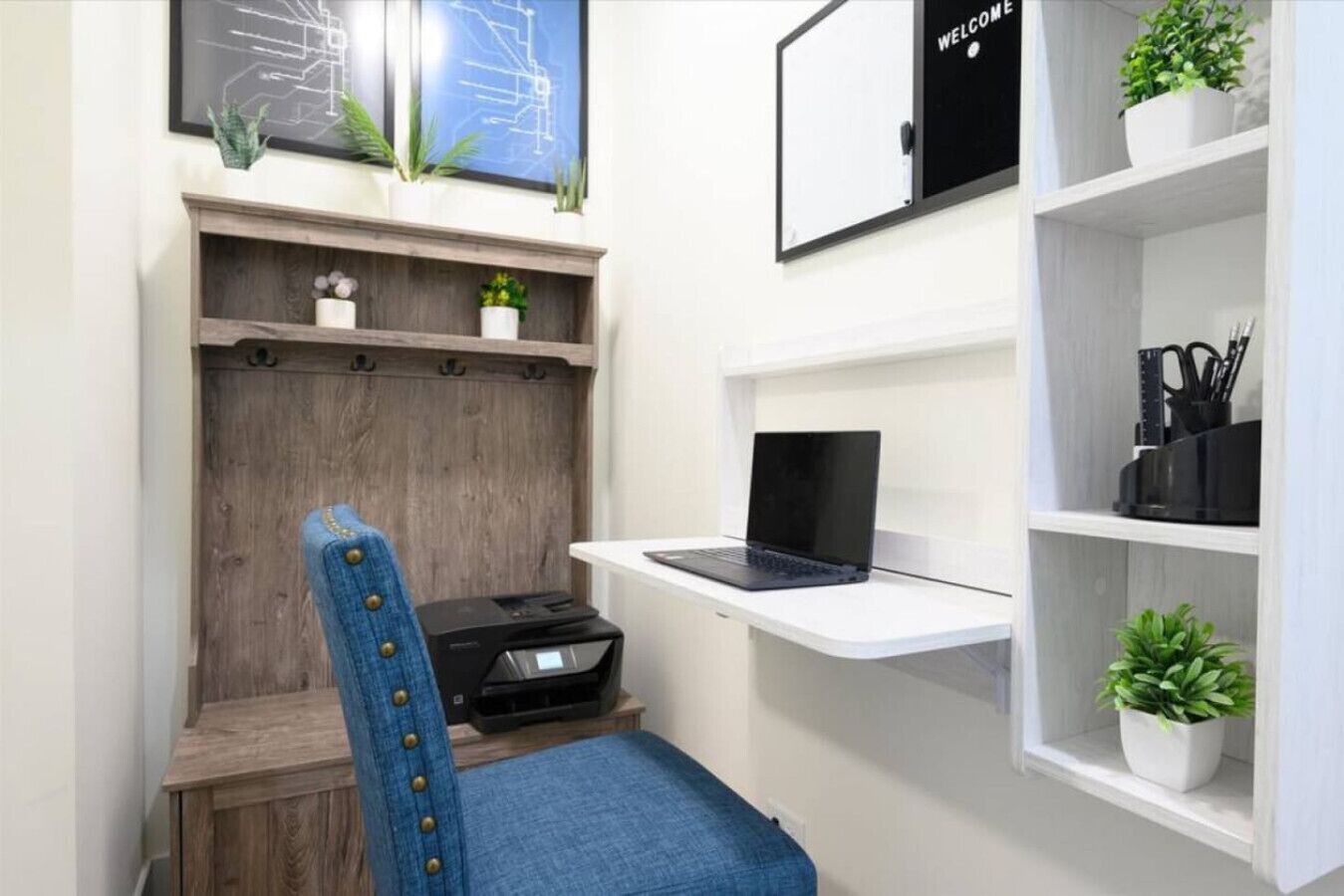 A home office setup with a desk, chair, laptop, printer, and shelving with plants.