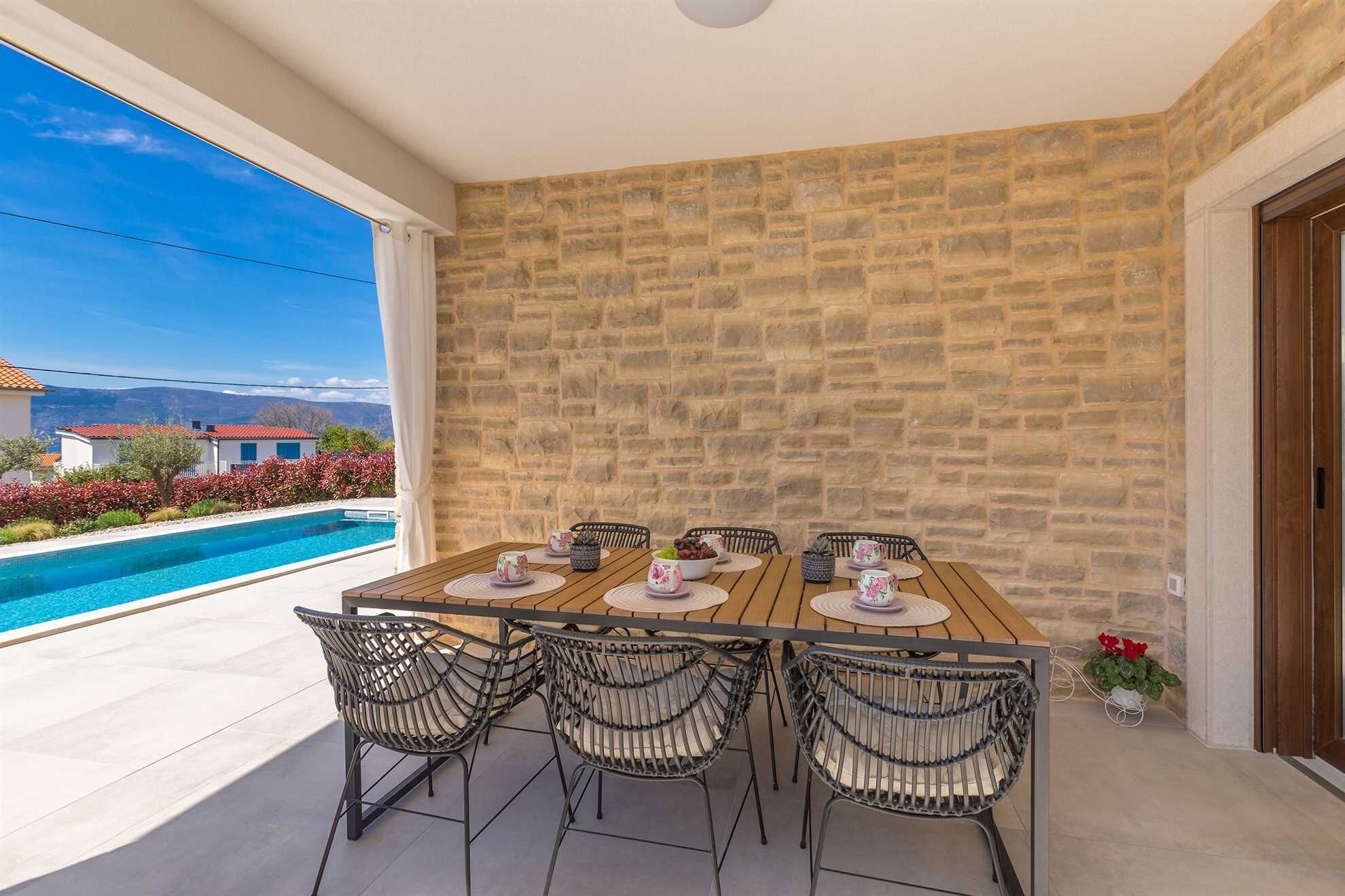 A dining area with a stone wall, a pool, and a view of houses.