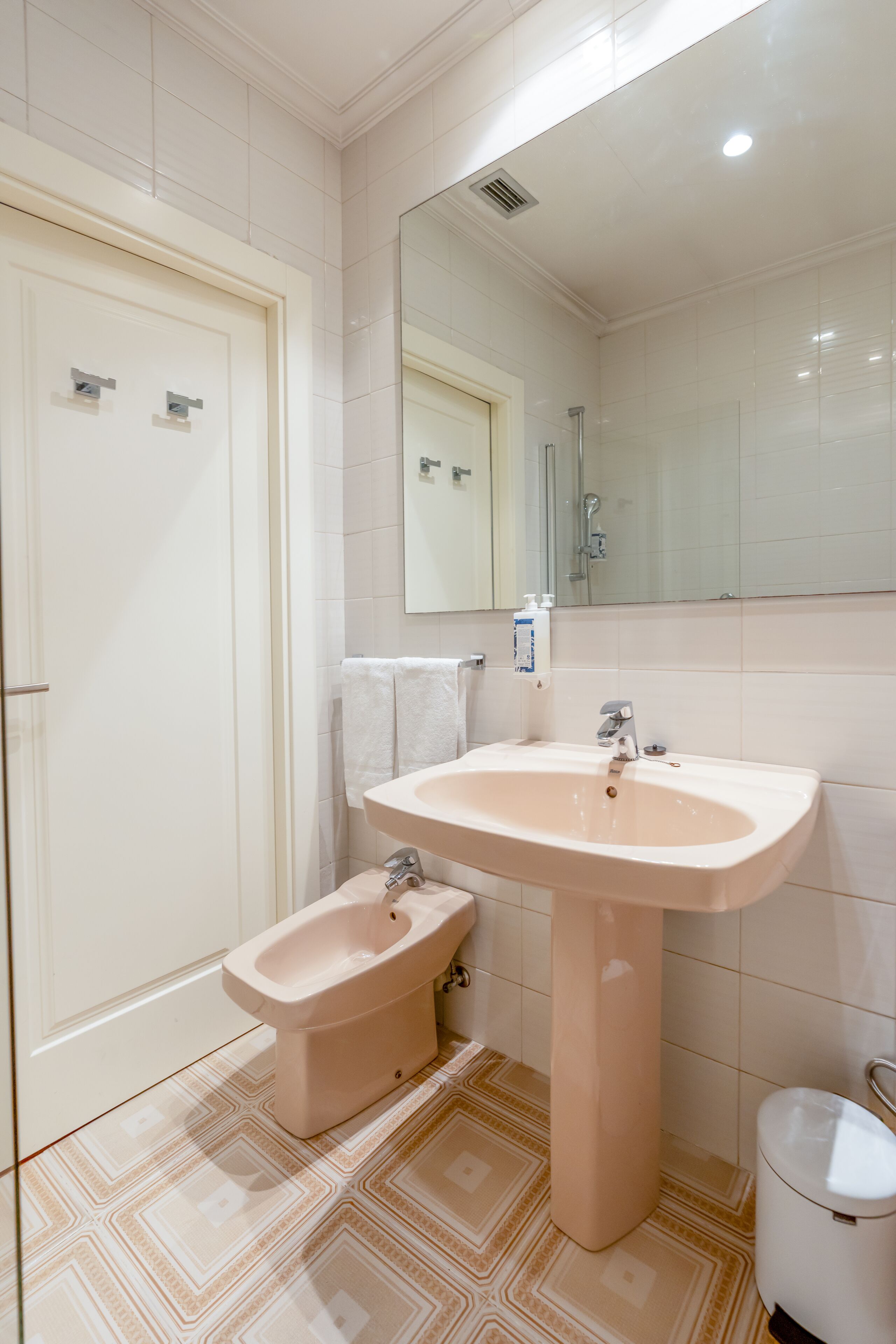A bathroom with a toilet, bidet, sink, mirror, and tiled floor.