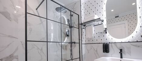 A modern bathroom with a glass-enclosed shower, a white marble floor, and a large mirror with a decorative frame.