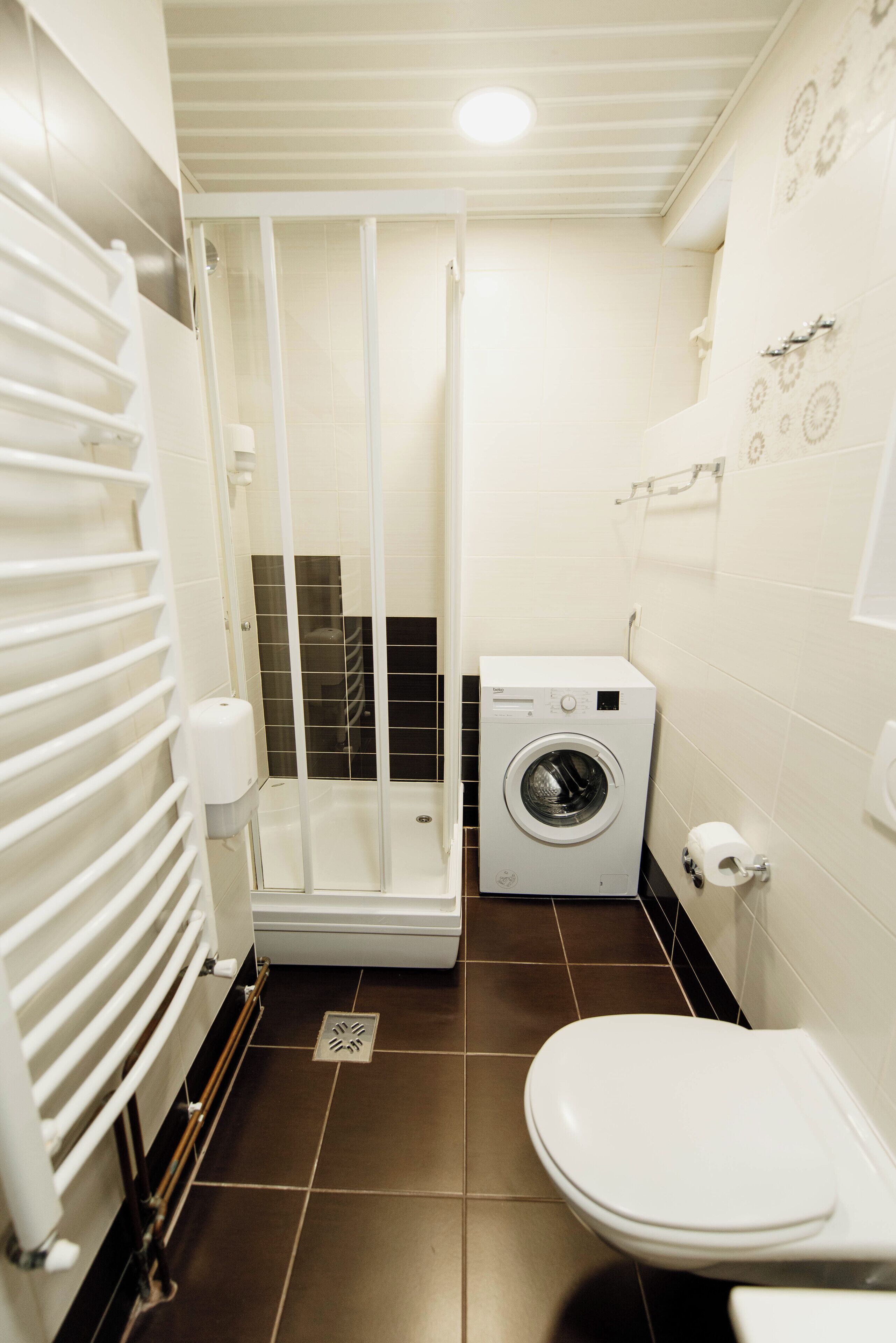 A compact bathroom with a shower, a washing machine, and a toilet.