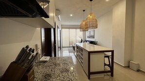 A modern kitchen with a granite countertop, a wooden island, and a hanging light fixture. - Ferrara Apartments (Mazatlán)