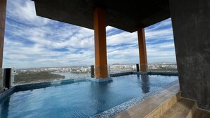 An infinity pool with a city view, supported by concrete pillars, and a clear sky. - Ferrara Apartments (Mazatlán)