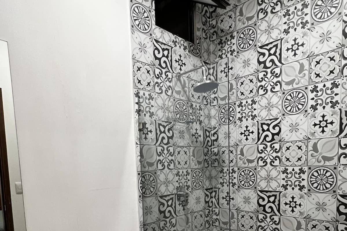 Casa de banho com sanita, lavatório e chuveiro com azulejos estampados.