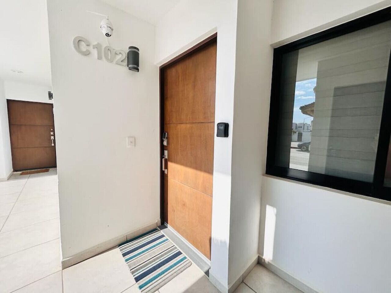 Un corridoio moderno con una porta in legno, un display digitale e una finestra che si affaccia all'esterno.
