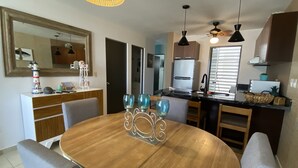 Un comedor con una mesa redonda de madera, sillas y un centro de mesa decorativo. Cuenta con una cocina que incluye un refrigerador, estufa y armarios.