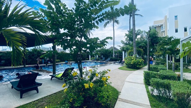 Zona de piscina con sillones de descanso, un espacio de estar cubierto y un jardín bien cuidado con flores amarillas.