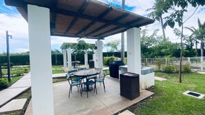 Un patio exterior con zona de estar cubierta, una parrilla y un contenedor de basura.
