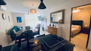 Una sala de estar moderna con comedor, una cocina con lavamanos y un dormitorio con cama y mesita de noche.
