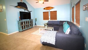 A living room with a dark blue couch, a wooden coffee table, a ceiling fan, and a mounted fish on the wall. - Welcome to Casa del Mar! Less than a mile away from beach! (Port Aransas)