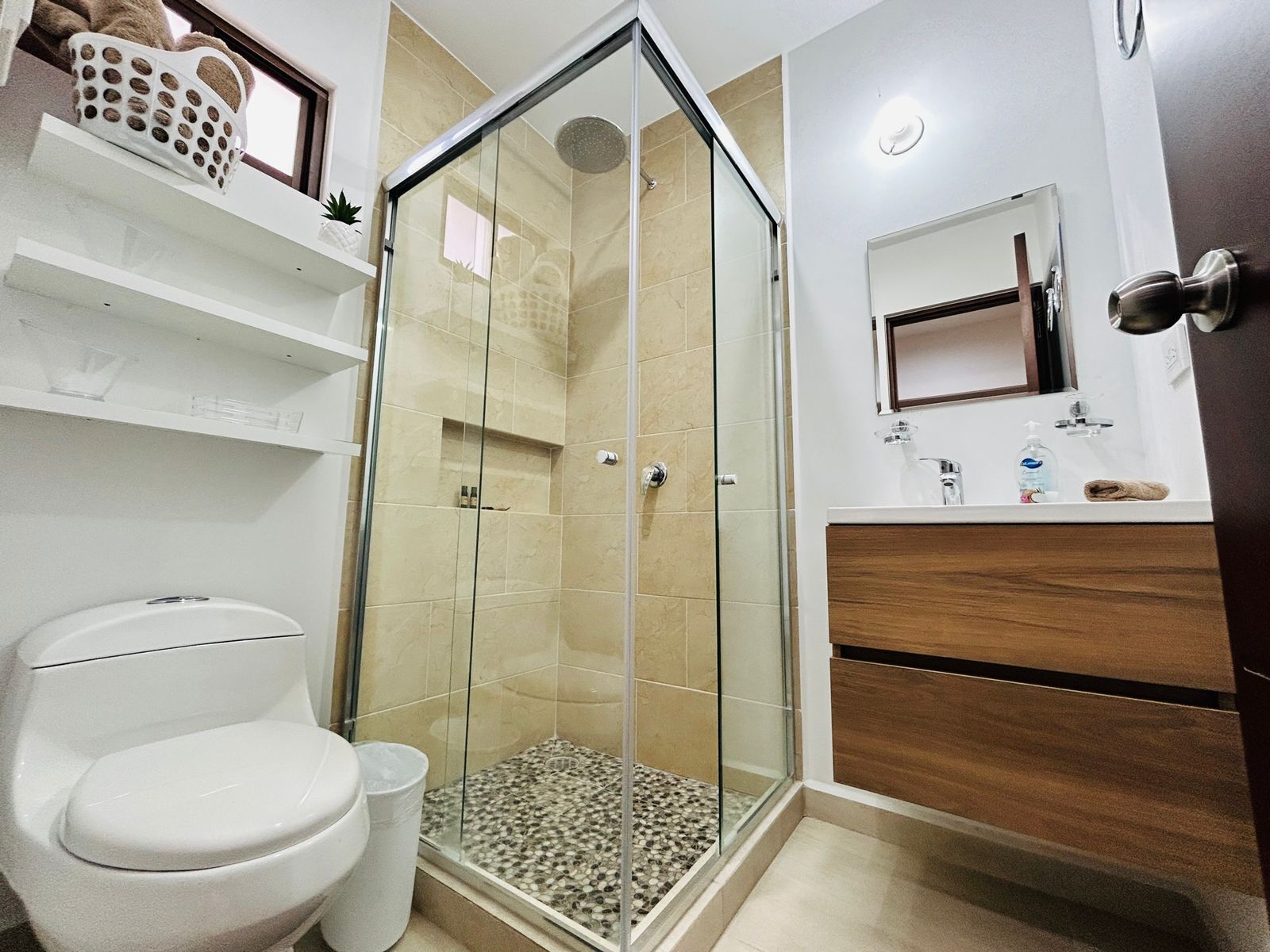 Un baño moderno con ducha de vidrio, inodoro y tocador con espejo.