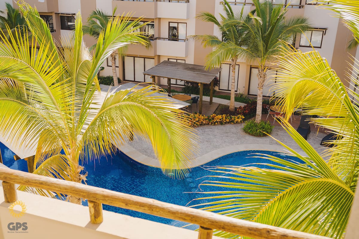 A pool area with palm trees, a covered seating area, and a building with balconies.