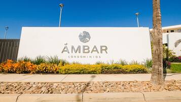 Señalización de 'ÁMBAR CONDOMINIOS' con un logotipo, rodeada de un área ajardinada con rocas y plantas.