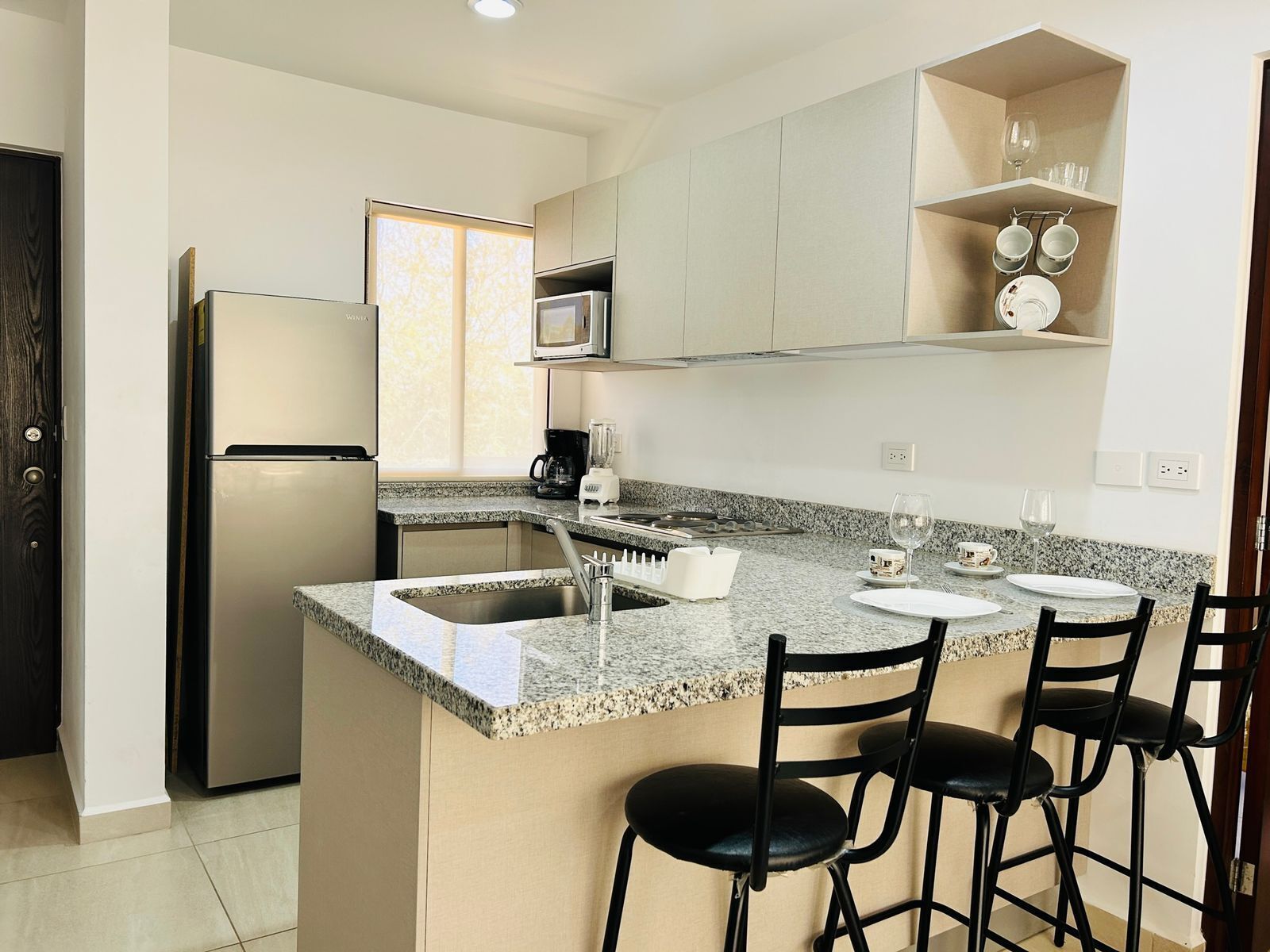 A modern kitchen with a refrigerator, microwave, sink, and bar stools.
