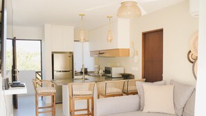 A modern kitchen with a central island, wooden chairs, and a sofa with cushions. - Ambar Apartments (Mazatlán)