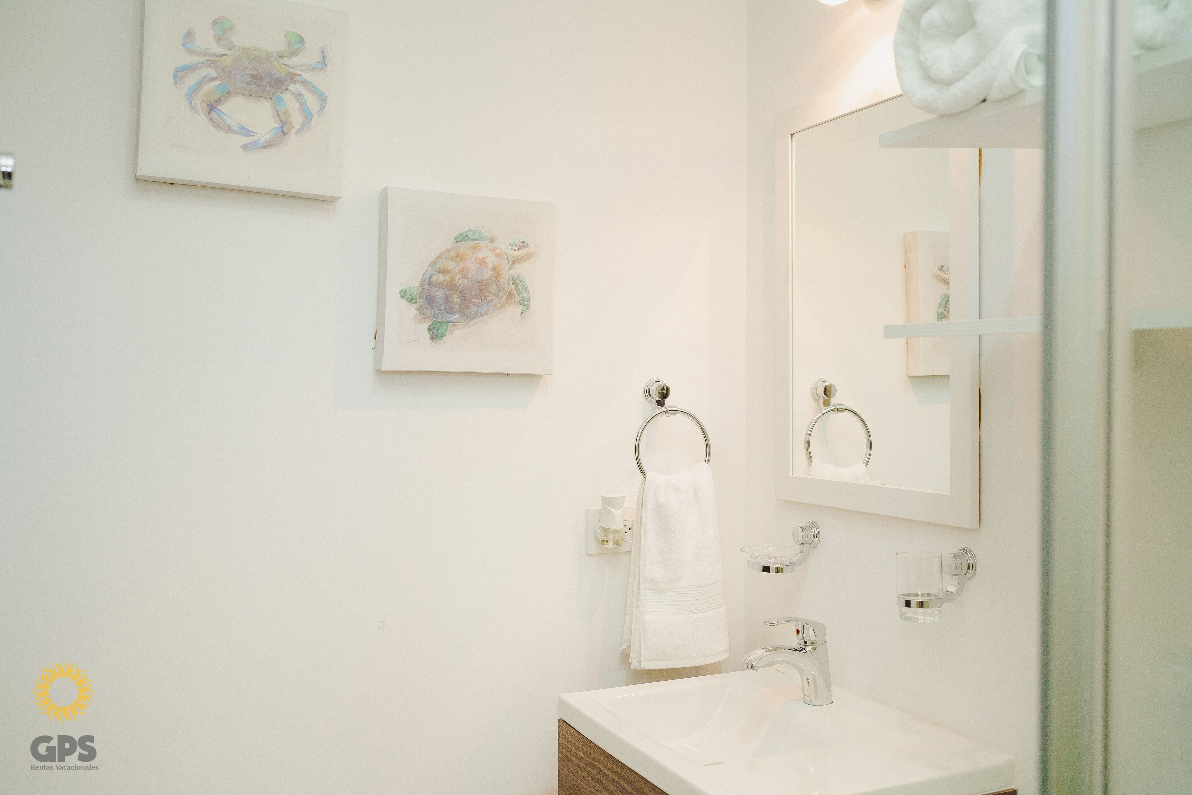 Un bagno con un lavandino bianco, uno specchio e due opere d'arte incorniciate raffiguranti un granchio e una tartaruga.