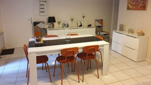 A dining area with a white table, four orange chairs, and a white cabinet in the background.