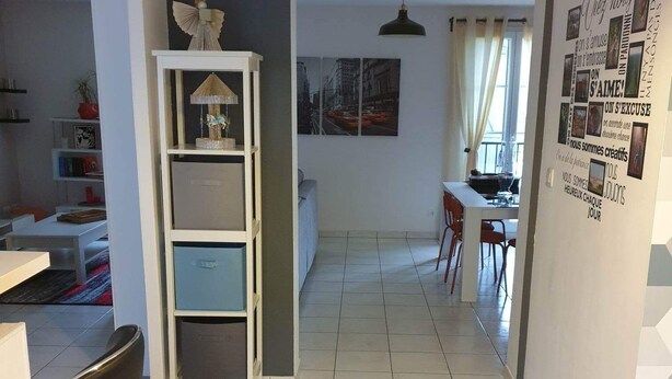 A modern kitchen with white cabinets, a dining area with a table and chairs, and a hallway leading to a living room.