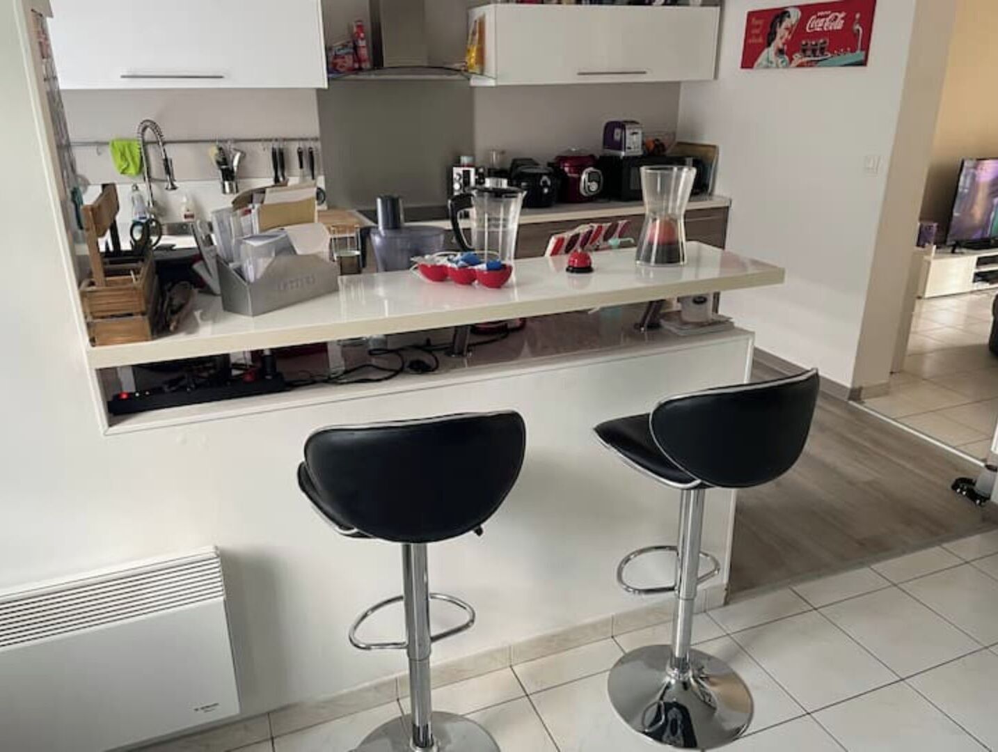 A modern kitchen with white cabinets, a white countertop, and two black bar stools.