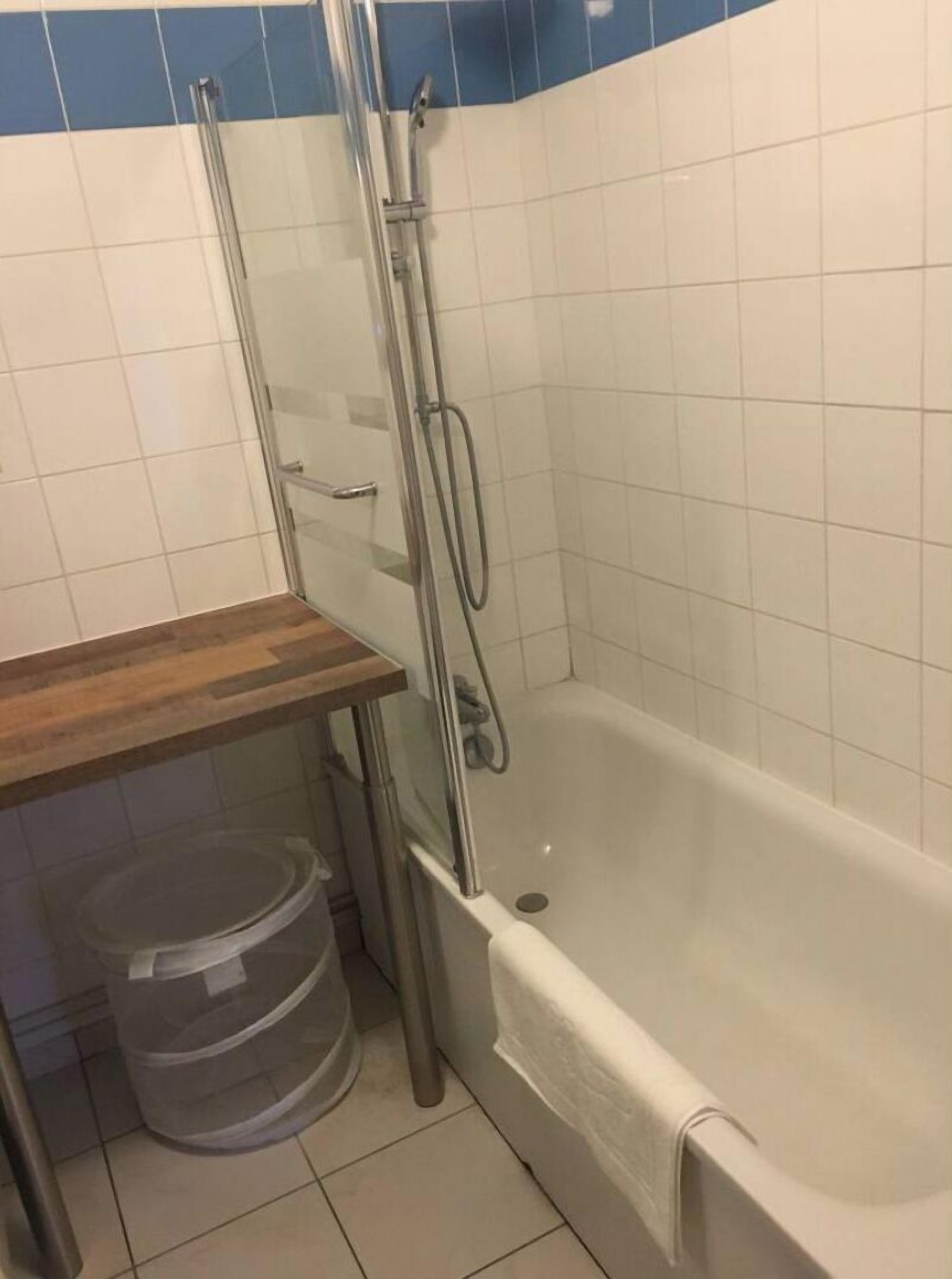 A bathroom with a glass-enclosed shower, a wooden vanity, and a plastic waste bin.