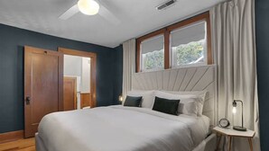 A bedroom with a large bed, a nightstand with a lamp, a window with curtains, and a ceiling fan. - Vitality Retreat - 1 block from DT/riverfront/shops/bars (Washington)