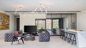 Una sala de estar moderna con un televisor de pantalla plana grande, sofás capitonados, una mesa de centro redonda y una lámpara de techo geométrica única.