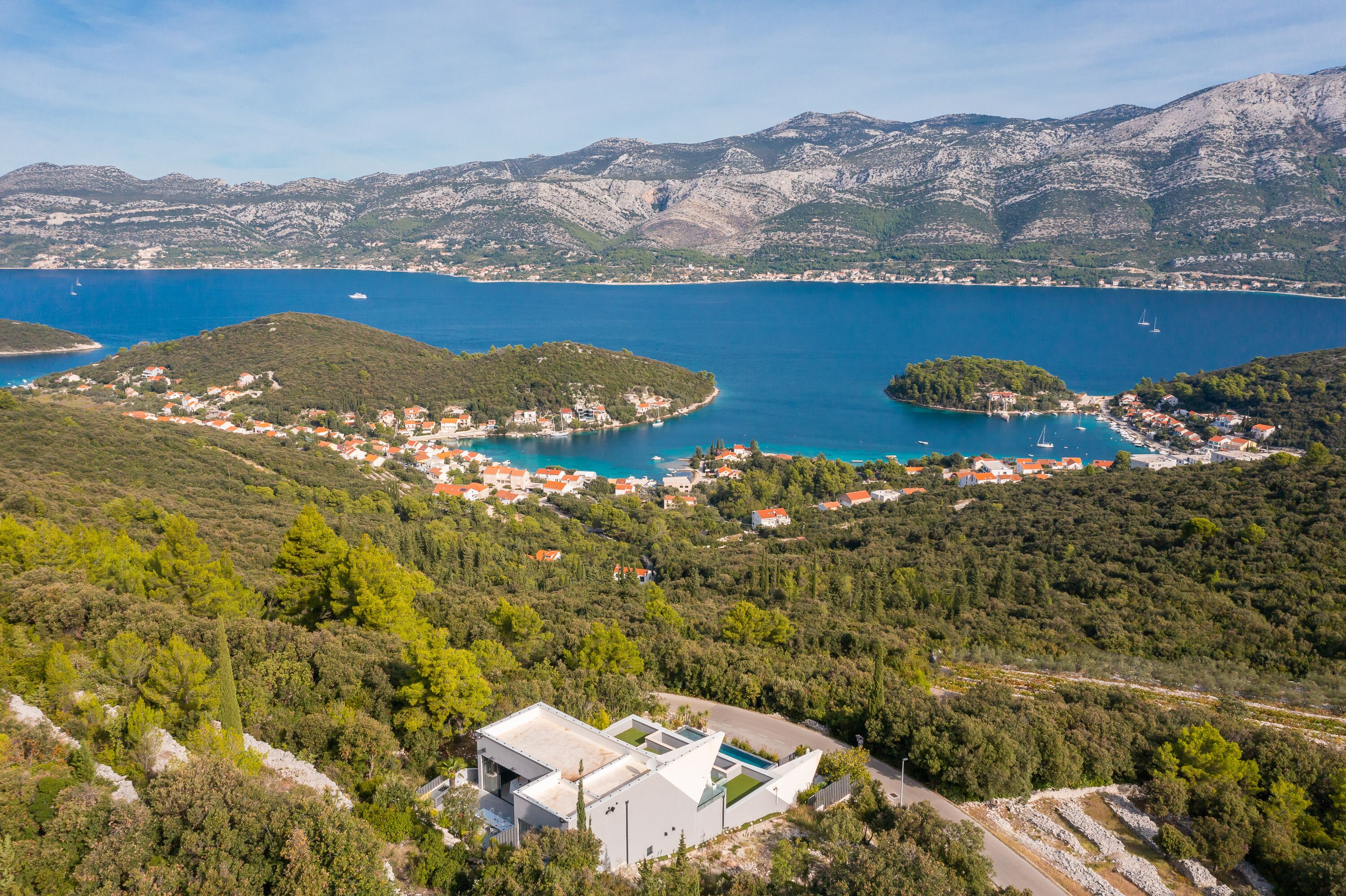 Une ville côtière dotée d’un port de plaisance, entourée de collines et bordée par une mer d’un bleu limpide.
