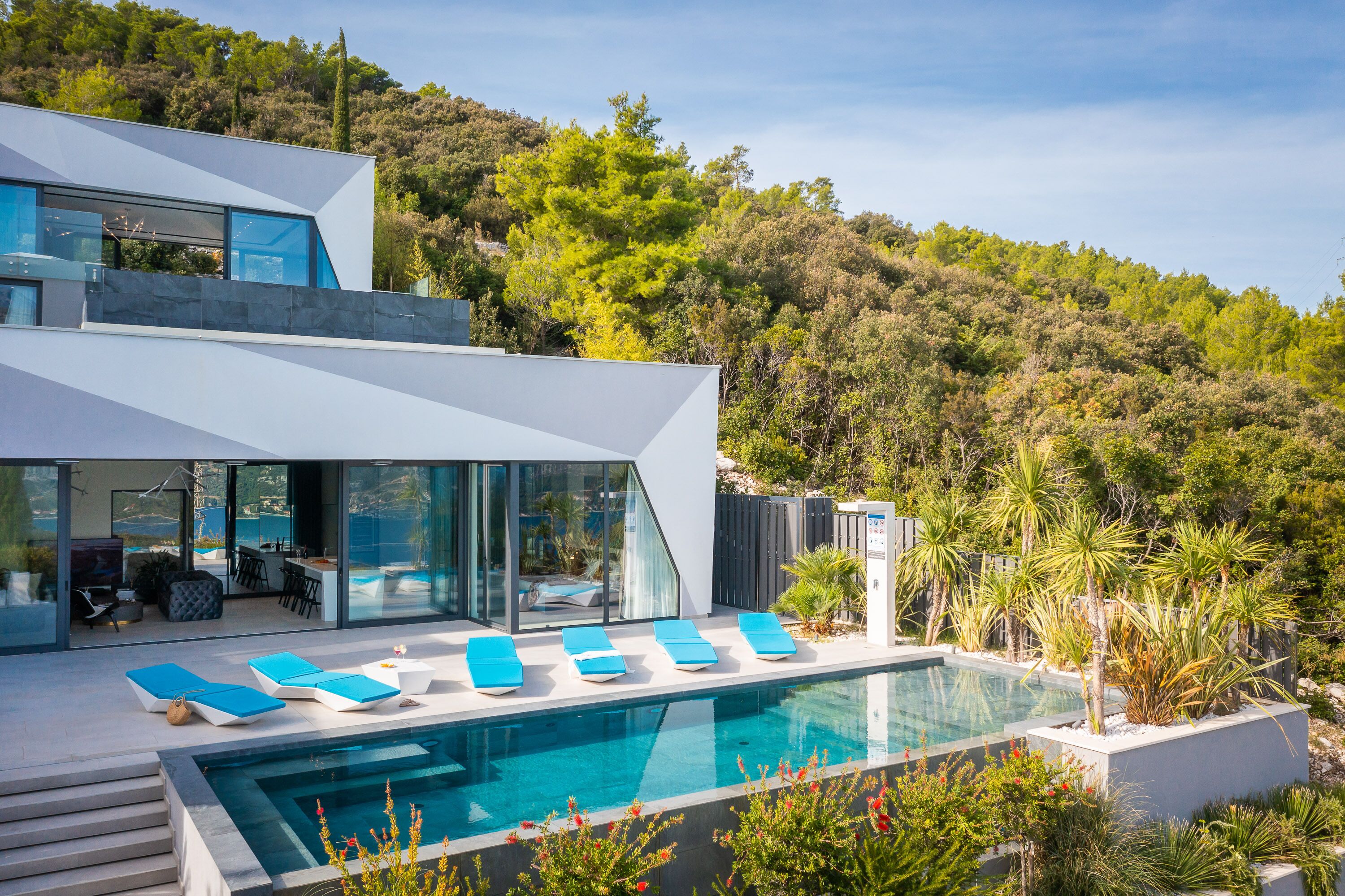 Ein modernes Haus mit Swimmingpool, Sitzgelegenheit im Freien und Blick auf einen bewaldeten Hang.