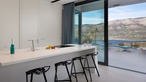 Una cocina moderna con una isla grande, taburetes de bar y vistas a montañas y un lago.