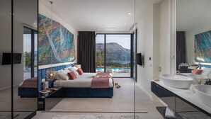Un dormitorio moderno con una cama grande, un baño con un lavamanos amplio y vistas a una montaña y una piscina.