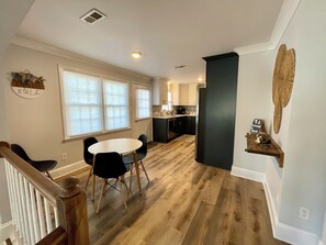 A modern kitchen with wooden flooring, a dining area with a round table and chairs, and a small island with a chalkboard sign. - Jewel on the Lake - Relaxing Lakefront Home (Manning)