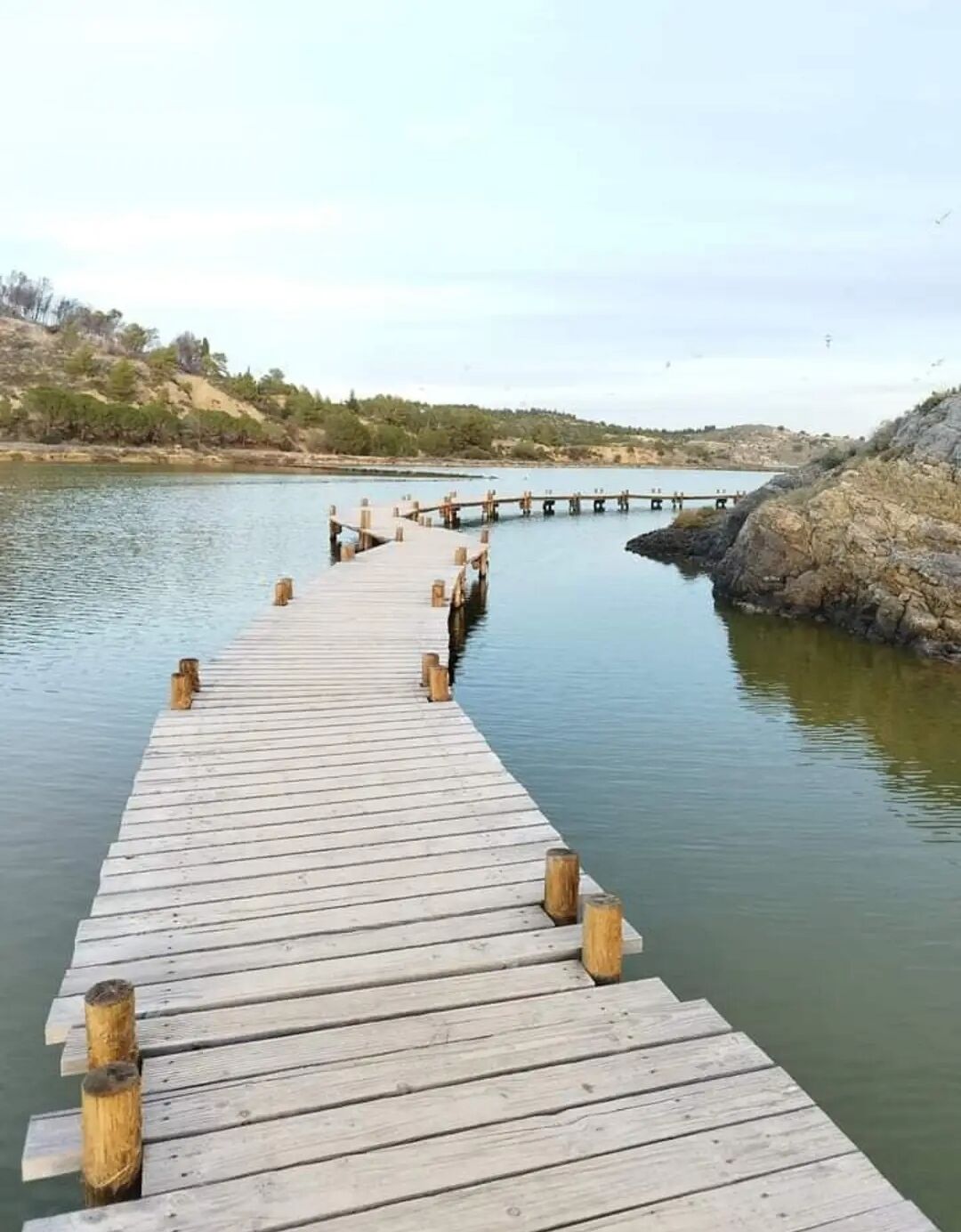 A wooden pier extending into calm water, surrounded by rocky terrain and sparse vegetation.