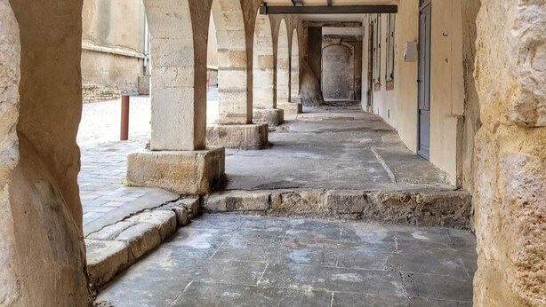 Un couloir bordé d’arches en pierre et doté d’un sol carrelé, qui mène à une porte au fond.