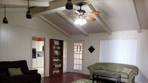 A spacious living room with a high ceiling, a ceiling fan, a bookshelf, a sofa, a coffee table, and a window with blinds. - Brooks Retreat: Swimming! Game Room! Staycation! (Richland Hills)