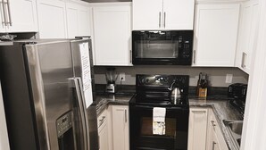 A compact kitchen with white cabinets, a stainless steel refrigerator, a microwave, and a black oven.