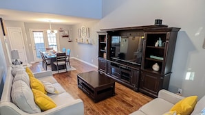 A spacious living room with a ceiling fan, wooden flooring, and a dining area with a table and chairs.