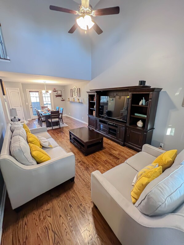Relax in this spacious living room with a high ceiling, ceiling fan, and comfortable sofa set.