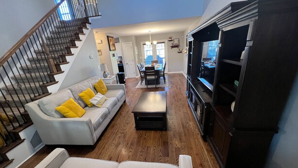 A spacious living room with a grey sofa, yellow cushions, a wooden coffee table, and a staircase with a railing.