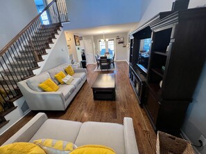 A spacious living room with a grey sofa, yellow cushions, a wooden coffee table, and a staircase with a railing.