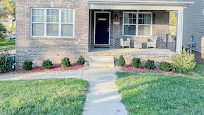 A two-story brick house with a front porch, a visible garage door, and a well-maintained lawn.