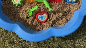 Ein blauer Sandkasten mit verschiedenen bunten Sandspielzeugen.