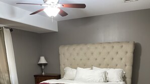 Una camera da letto con un letto, una ventola a soffitto, un comodino e una lampada da terra.