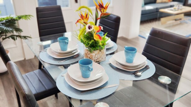 Een moderne eethoek met een glazen tafel, zwarte stoelen en blauwe bekers.