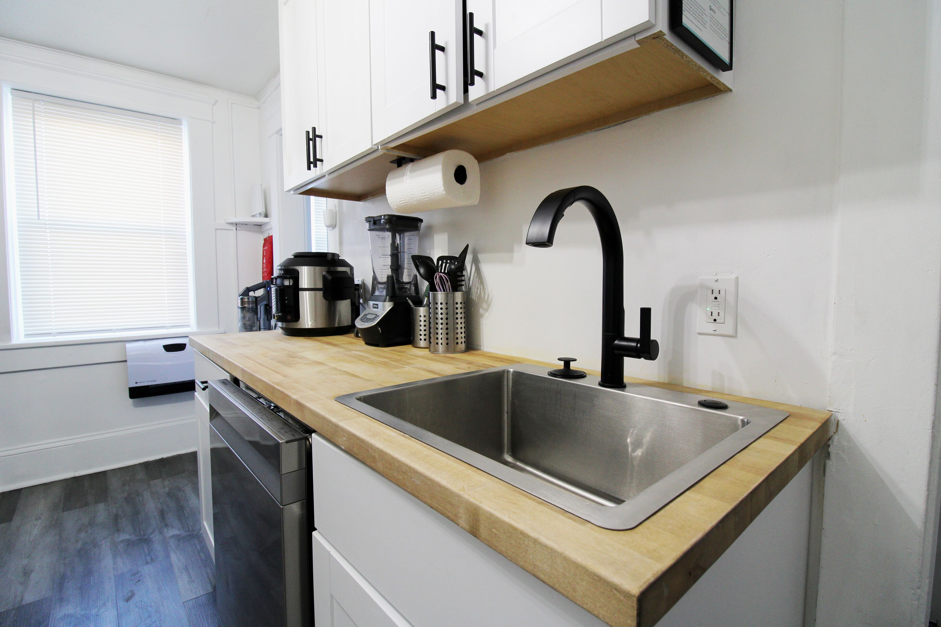 Eine moderne Küche mit Spüle aus Edelstahl, einer Holz Arbeitsplatte und weißen Schränken.