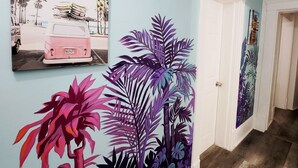 Een gang met een lichtblauwe wand, een deur en een groot muurschildering met tropisch thema.